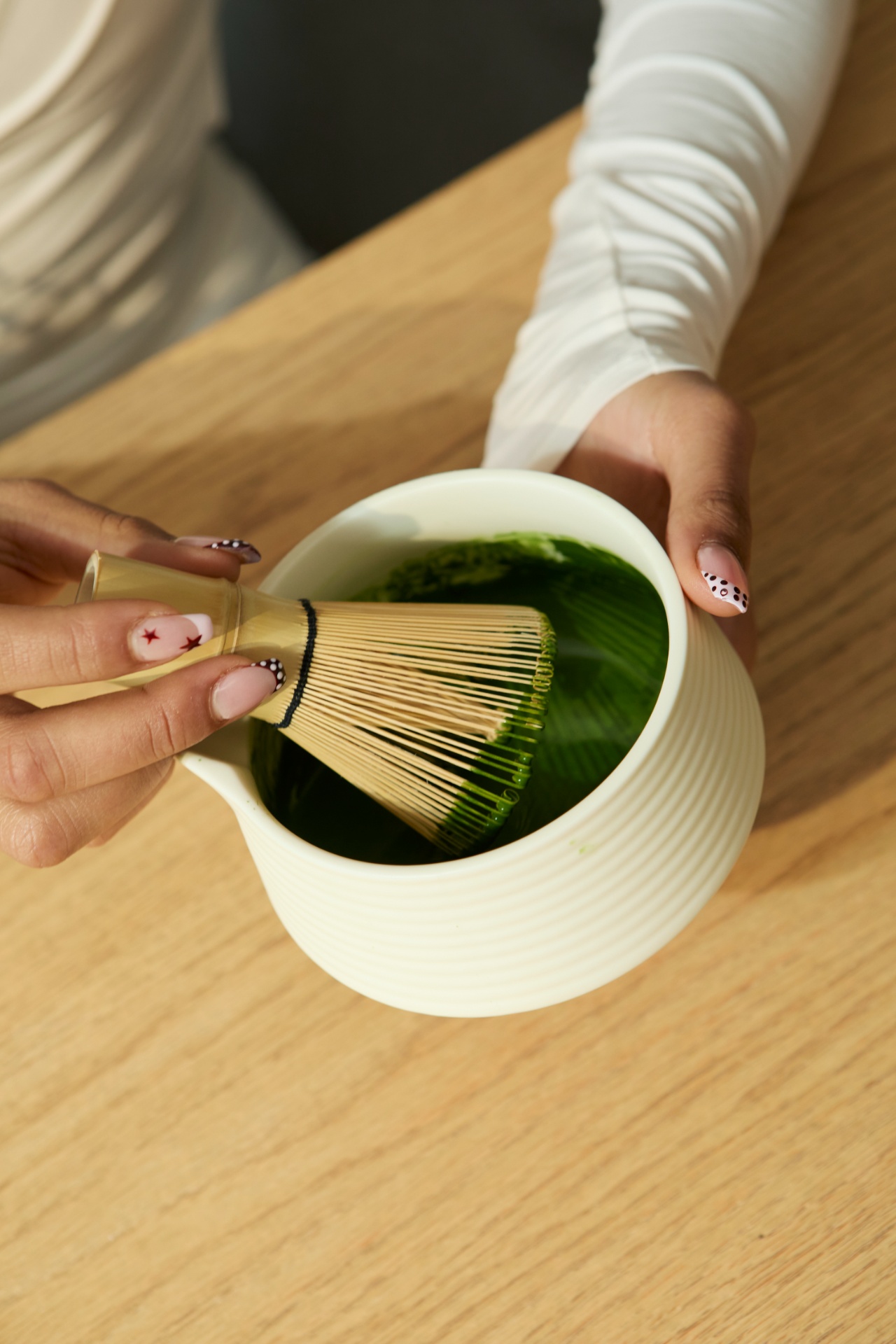 Hands whisking matcha in a cream bowl on a wood table