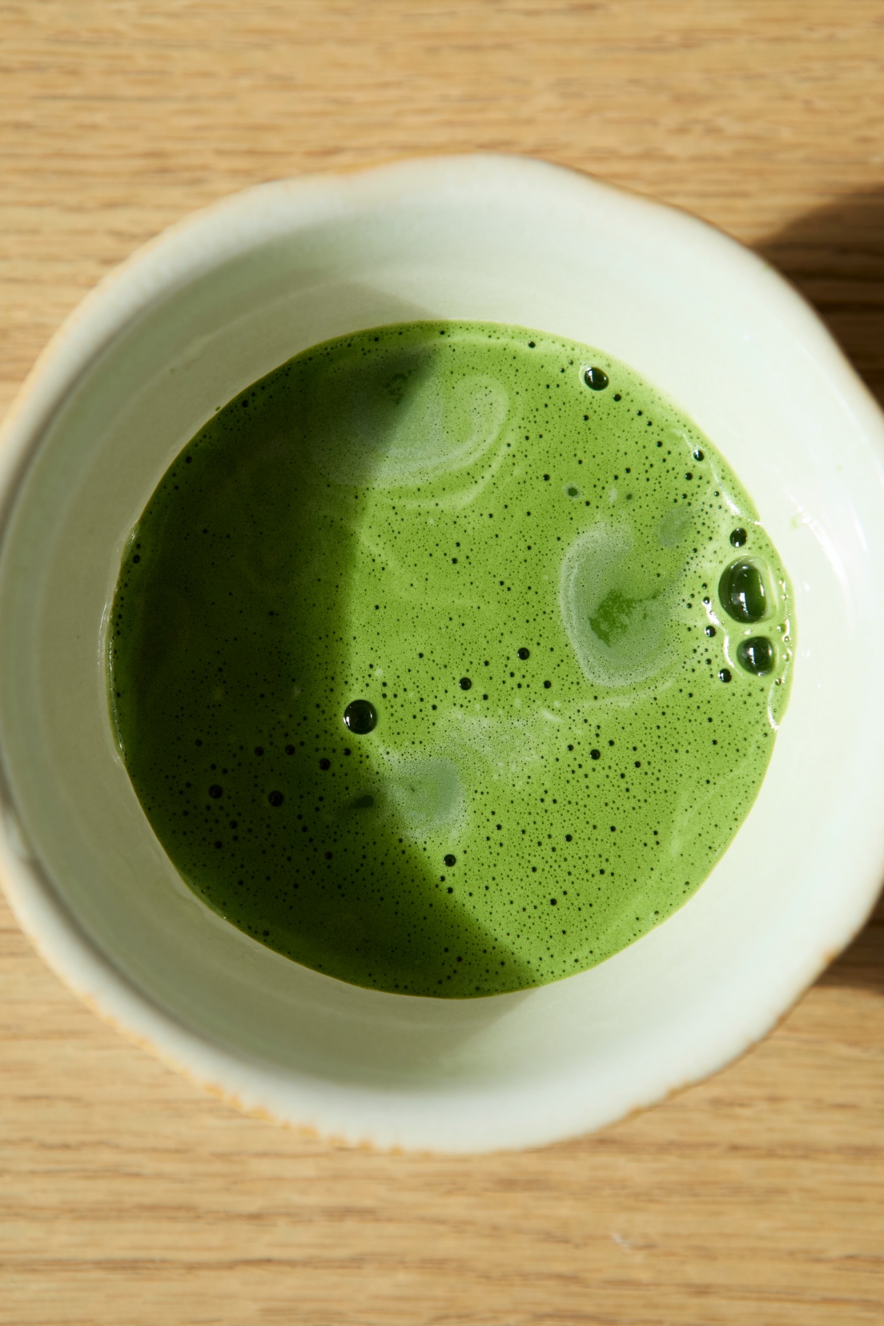 Bowl of whisked matcha photographed from above on a light wood table