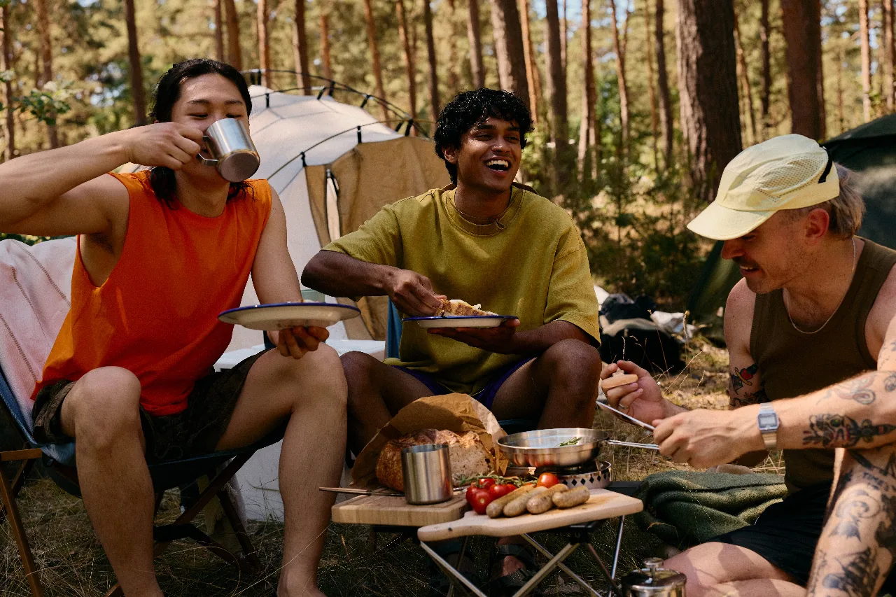 Three friends eating breakfast on camp chairs outside a tent in a pine forest