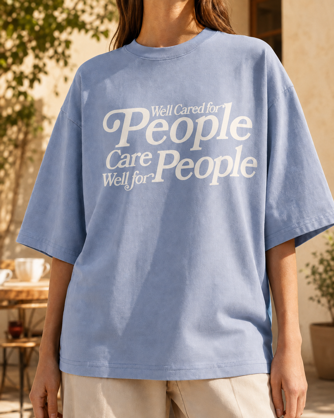 A woman wearing a light blue tee reading Well Cared for People Care Well for People