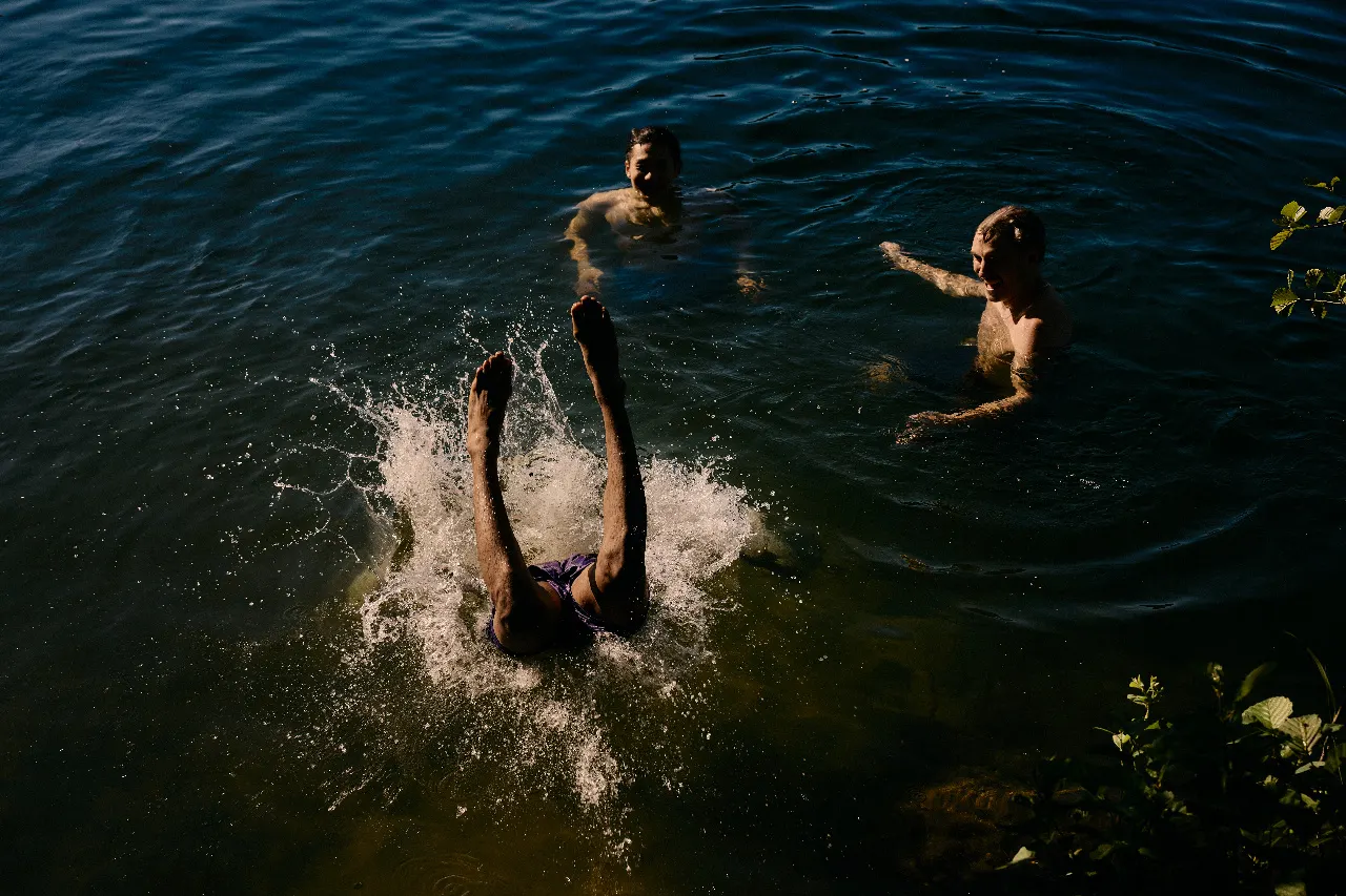 Friends swimming in a dark lake, one of them mid-dive with a splash