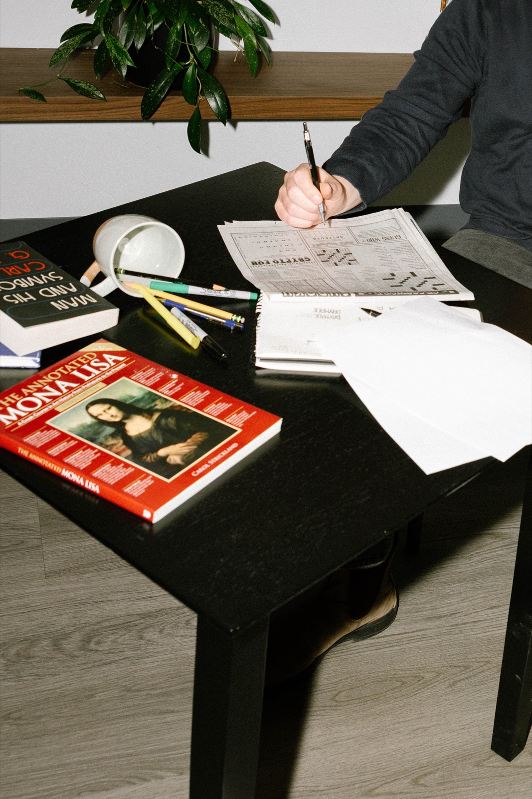 Quinn's work table with books, pens, and a crossword